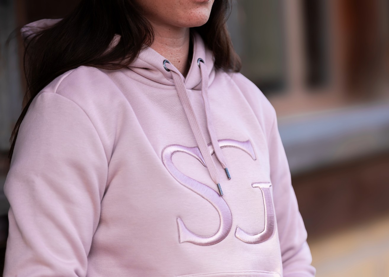 Haut à capuche rose pâle avec broderie en relief "SJ" sur le torse, proches cordons et œillets argentés.