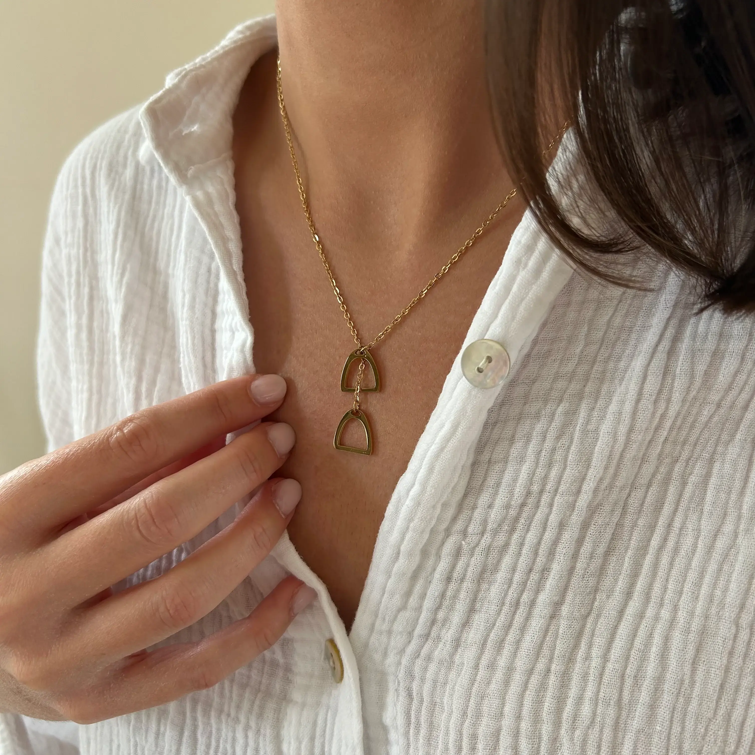 Collier orné de deux pendentifs en forme d'arche dorée, porté sur une chemise blanche côtelée.